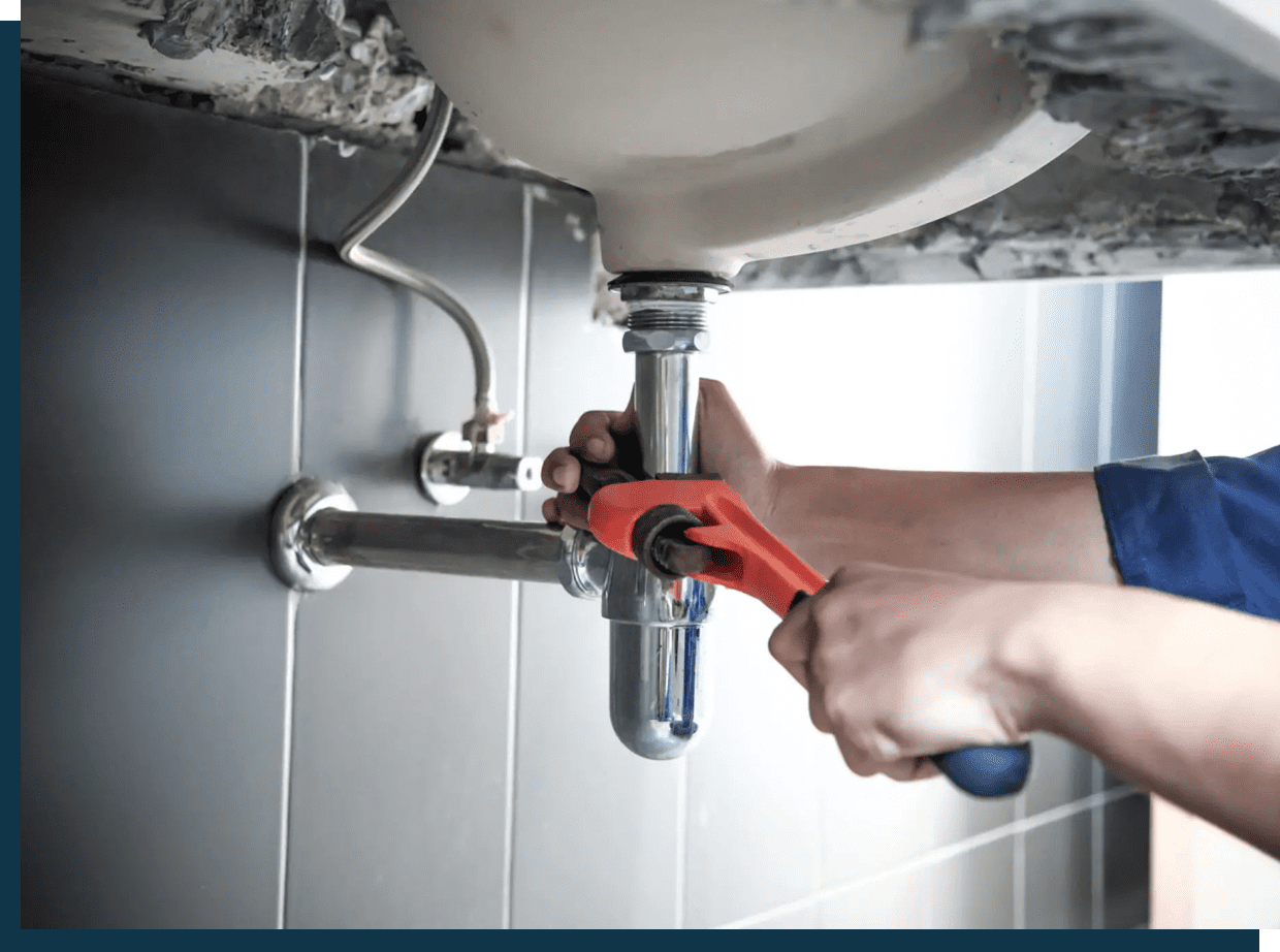 A person using a wrench to fix a pipe under a sink.